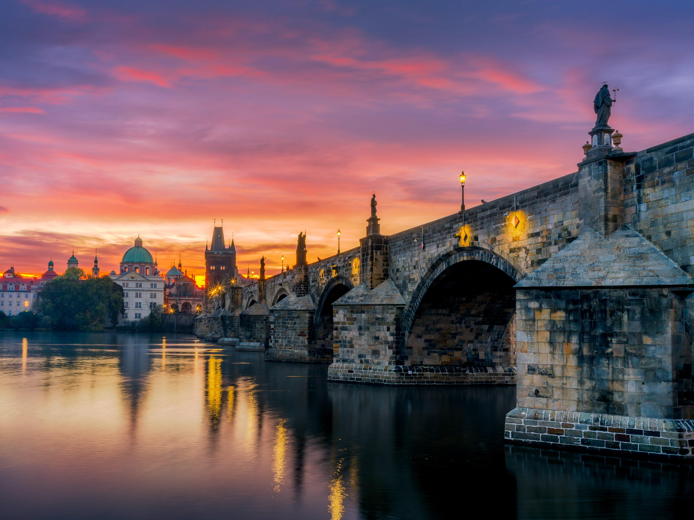 Charles Bridge piers and lamplight lead to the Old Town Bridge Tower at dawn in Prague, Czech Republic. Cityscape photography by Jonathan Gardner.